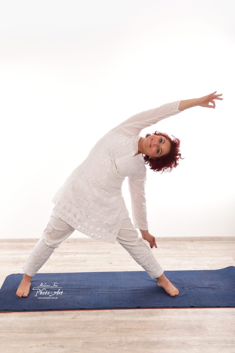 Frau in weißem Outfit macht seitliche Dehnübung auf Yogamatte.