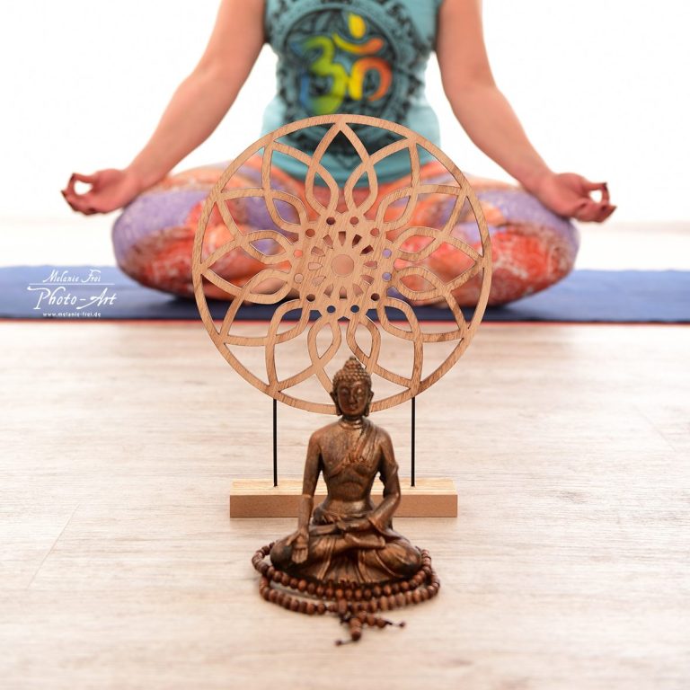 Eine sitzende Person meditiert vor einer Holzskulptur und einem Buddha.