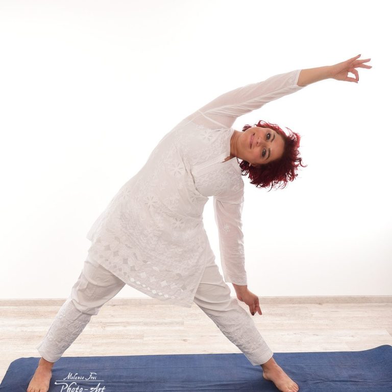 Eine Frau in weißer Kleidung macht eine Yoga-Dehnübung auf einer Matte.